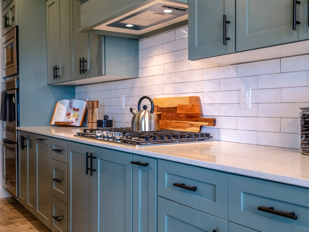 Blue kitchen cabinets with white backsplash, gas stovetop, and stainless steel kettle.