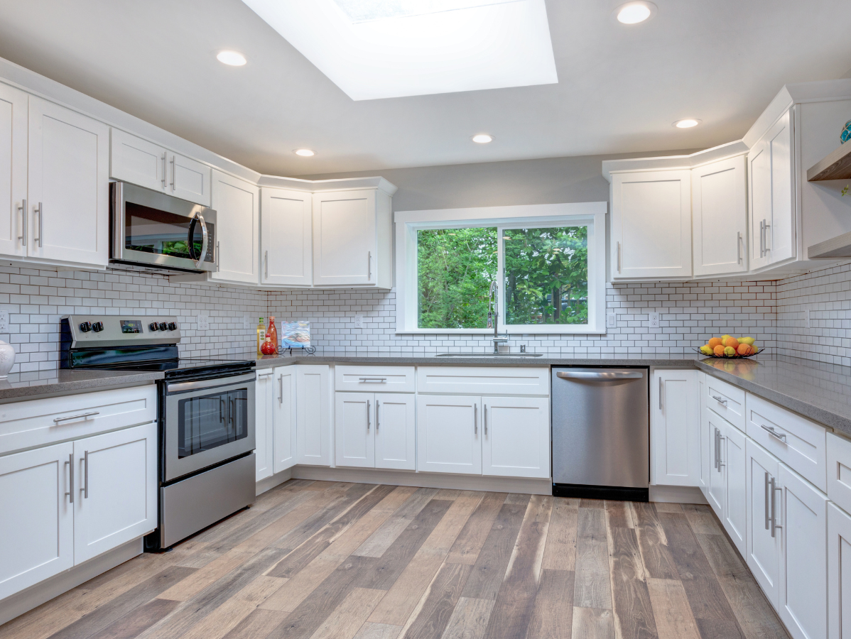 White kitchen with stainless steel appliances, gray countertops, and wood-look flooring.