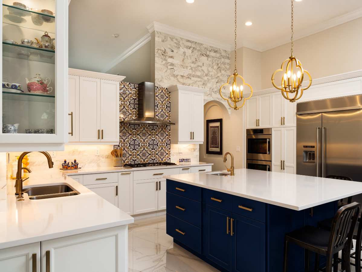 A modern kitchen with white cabinets, blue island, brass fixtures, and a stone accent wall.