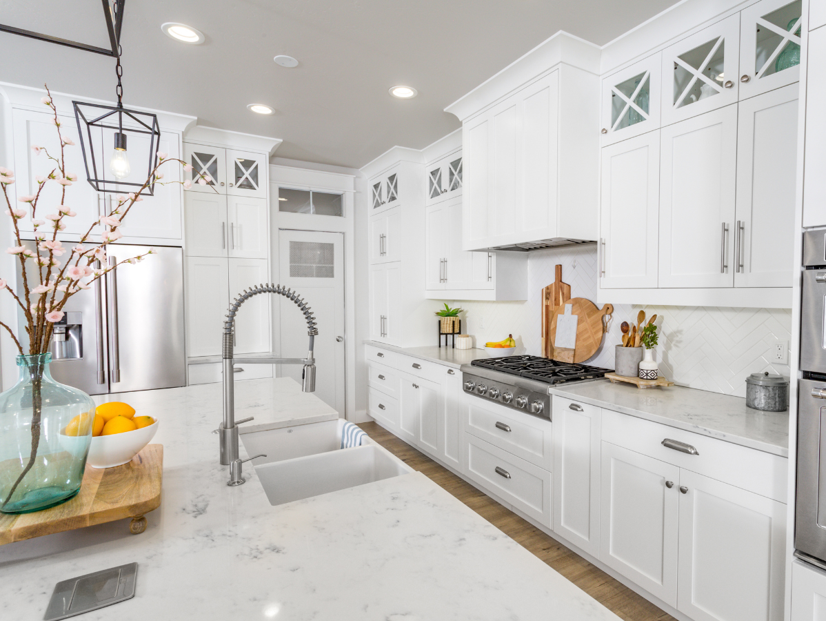 Bright white kitchen with an island, stainless steel appliances, and overhead lighting.
