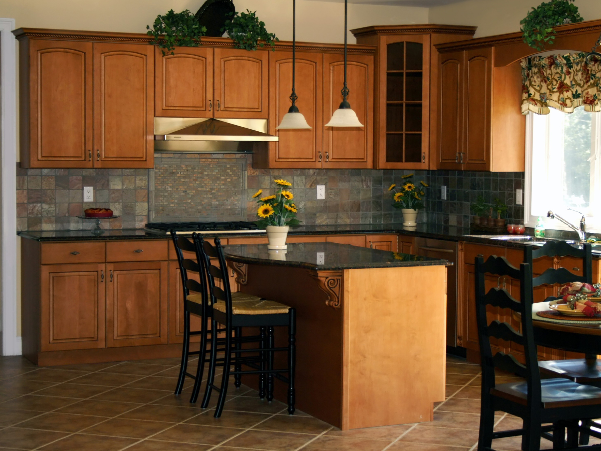 Kitchen with brown cabinets, granite countertops, island, and dark chairs.