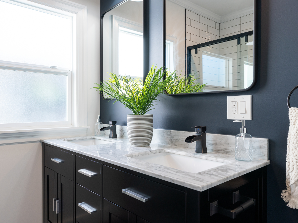 Bathroom with black vanity, marble countertop, black fixtures, mirror, and plant. Dark blue wall.