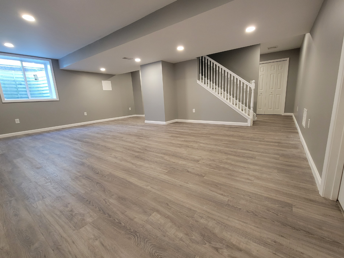 Spacious basement with gray walls, light wood-look flooring, a staircase, and recessed lighting.