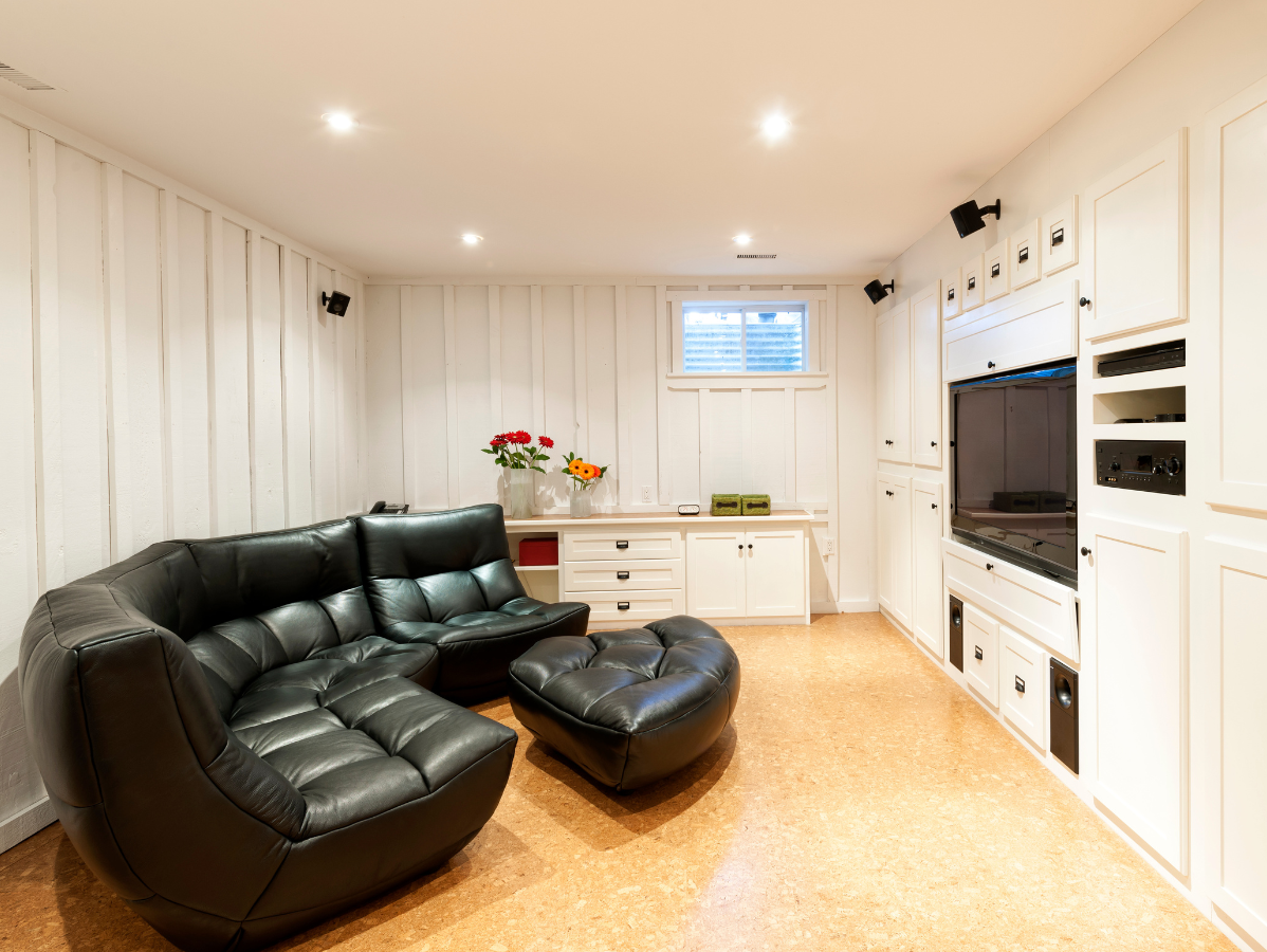Black leather sectional in a white-walled room with a built-in entertainment center, cork flooring.