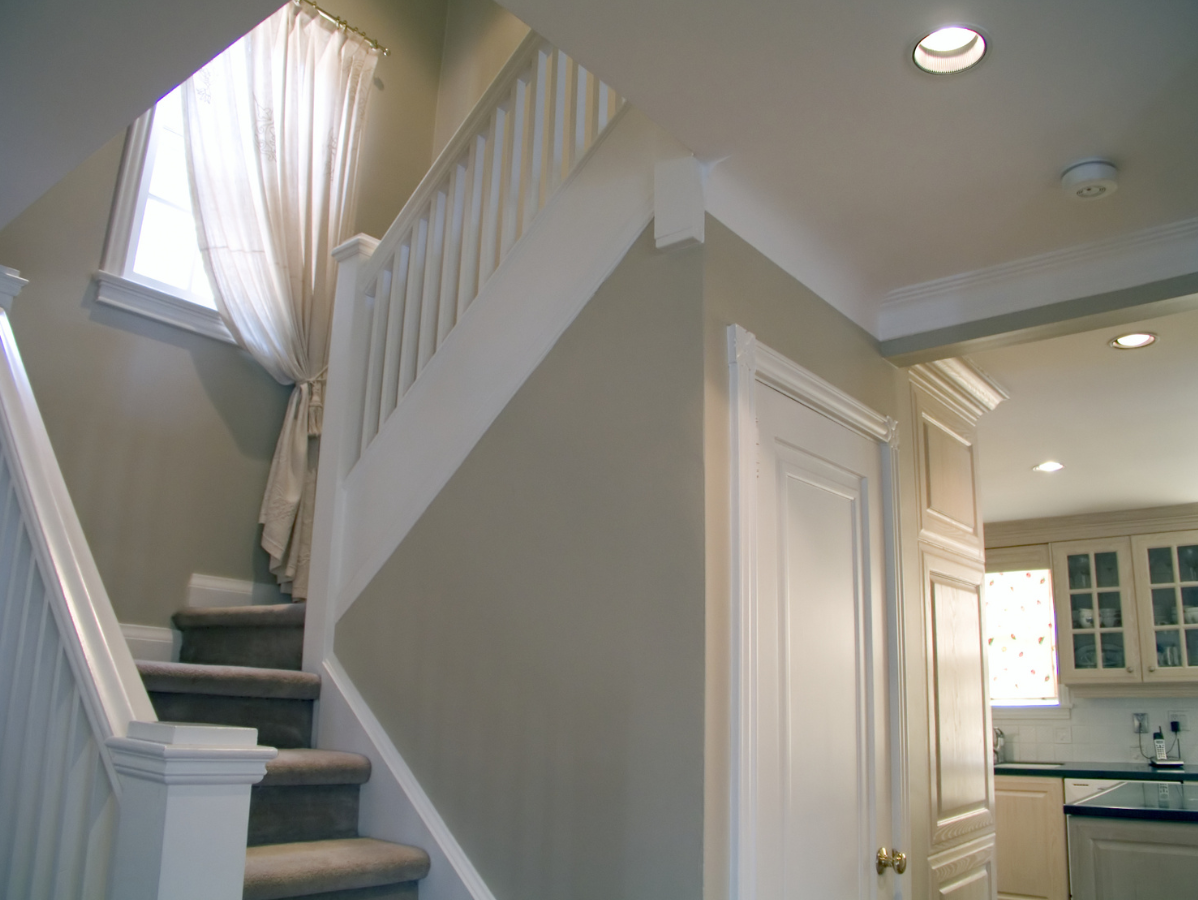 Staircase with white banister and tan wall, leading up to a window with sheer curtains; next to white door.