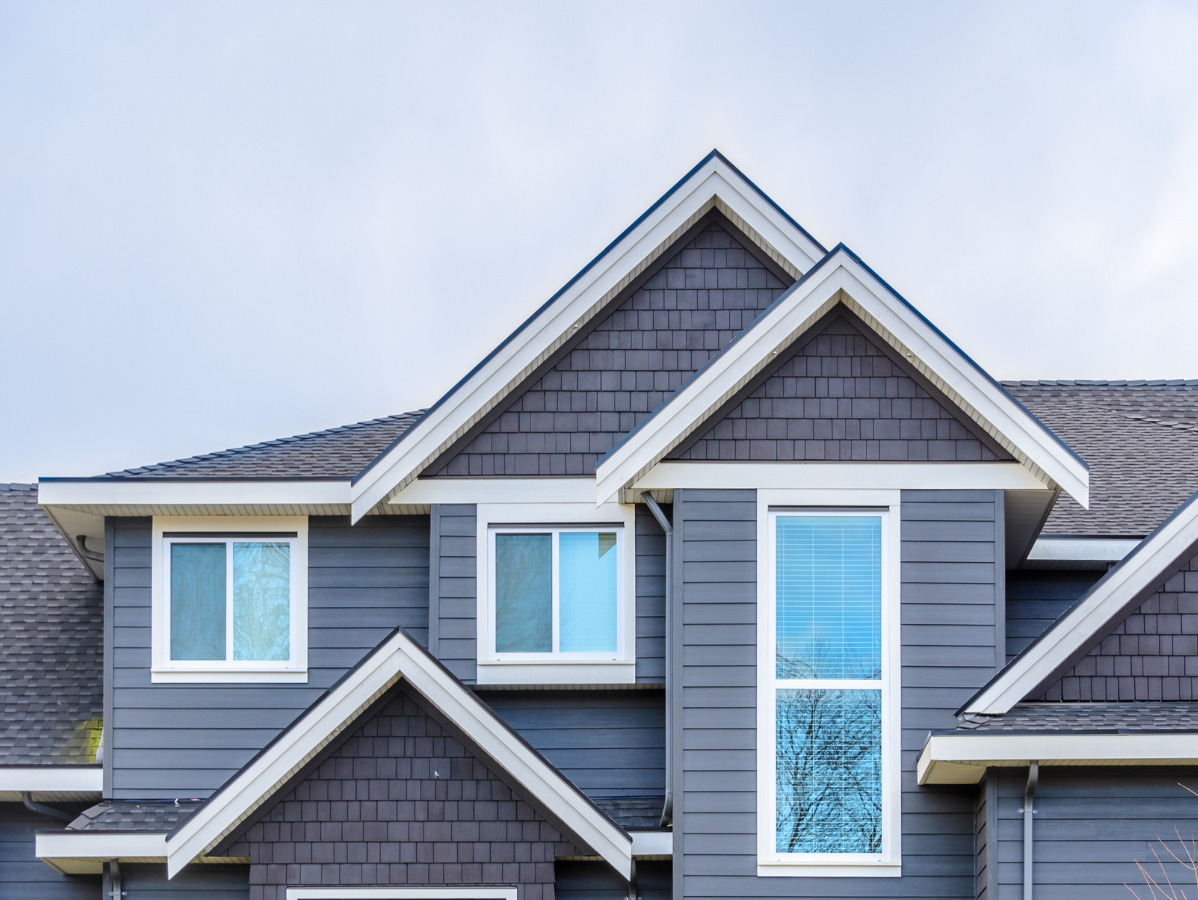 Gray house with gabled roof, white trim, and windows against a cloudy sky.