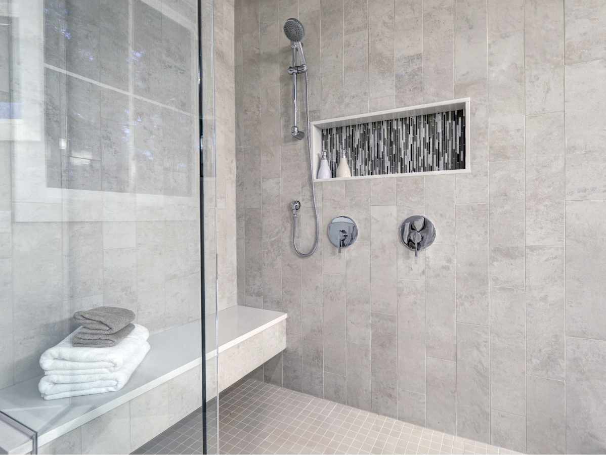 Modern shower with gray tiled walls, glass door, built-in bench, and decorative niche.