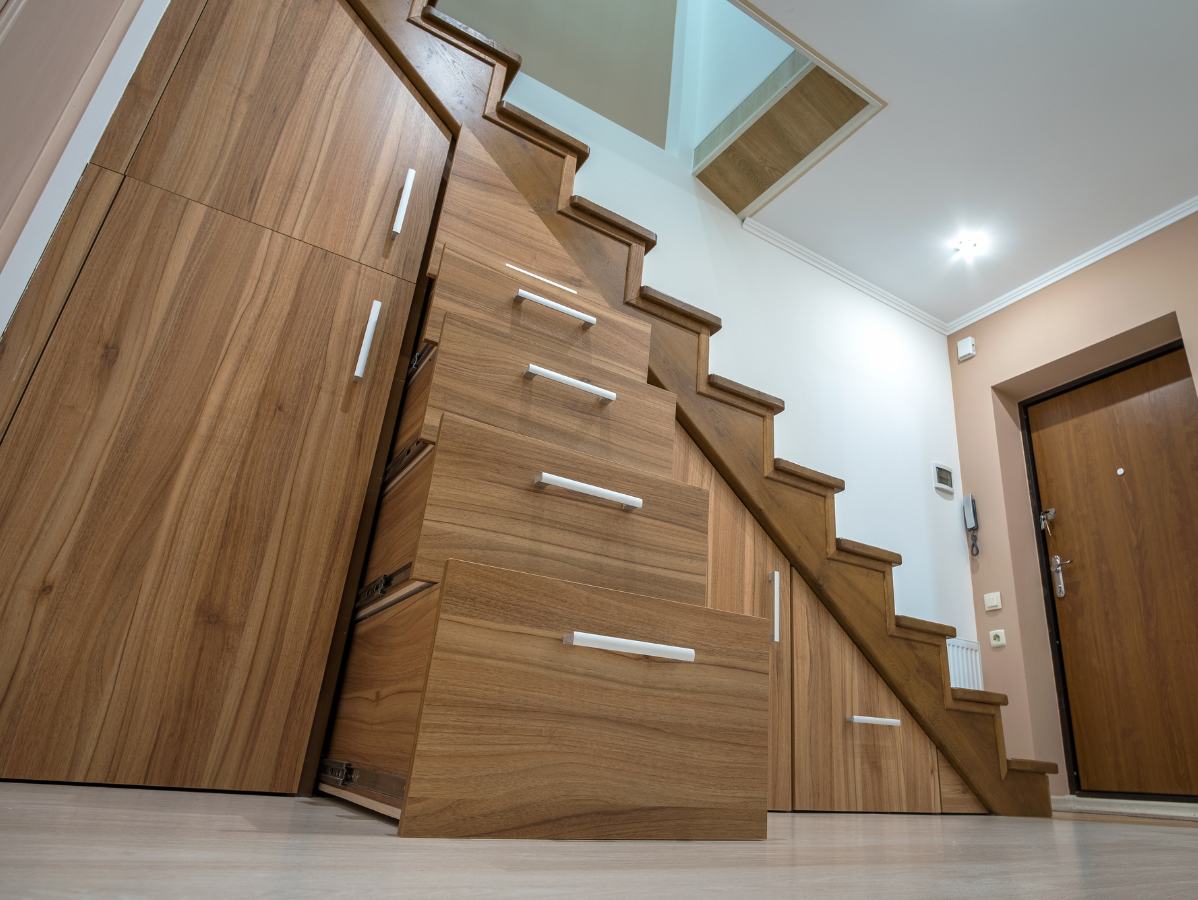 Wooden staircase with built-in storage, including drawers and cabinets. Entrance hall with a door and light fixtures.