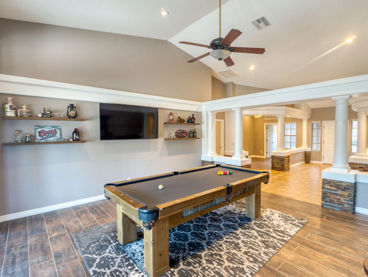 Pool table in a game room with shelves, a TV, and a light brown ceiling.