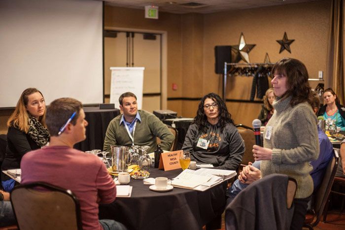 A group of people are sitting around a table with a woman holding a microphone.