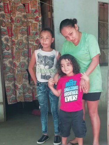 A woman stands next to two children one of whom is wearing a shirt that says most amazing brother ever