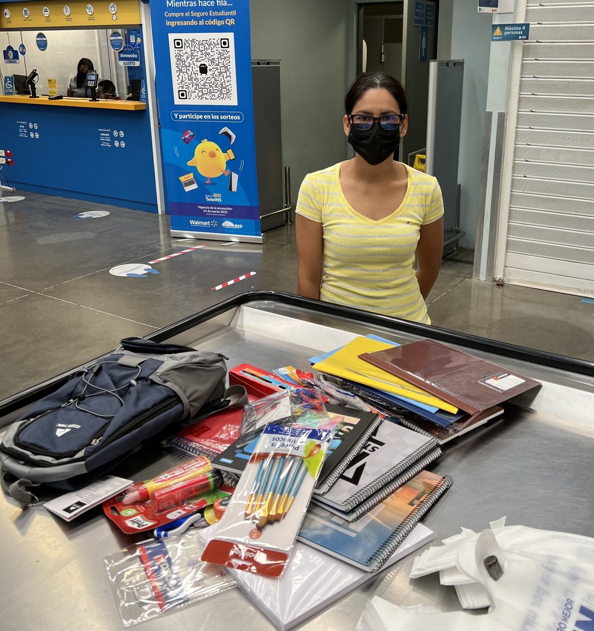 A woman wearing a mask stands in front of a counter full of school supplies