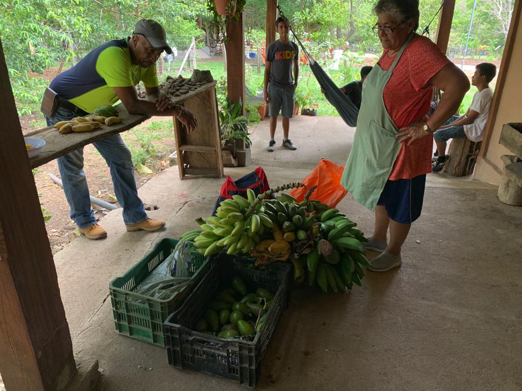 A woman is standing next to a bunch of bananas on a porch.