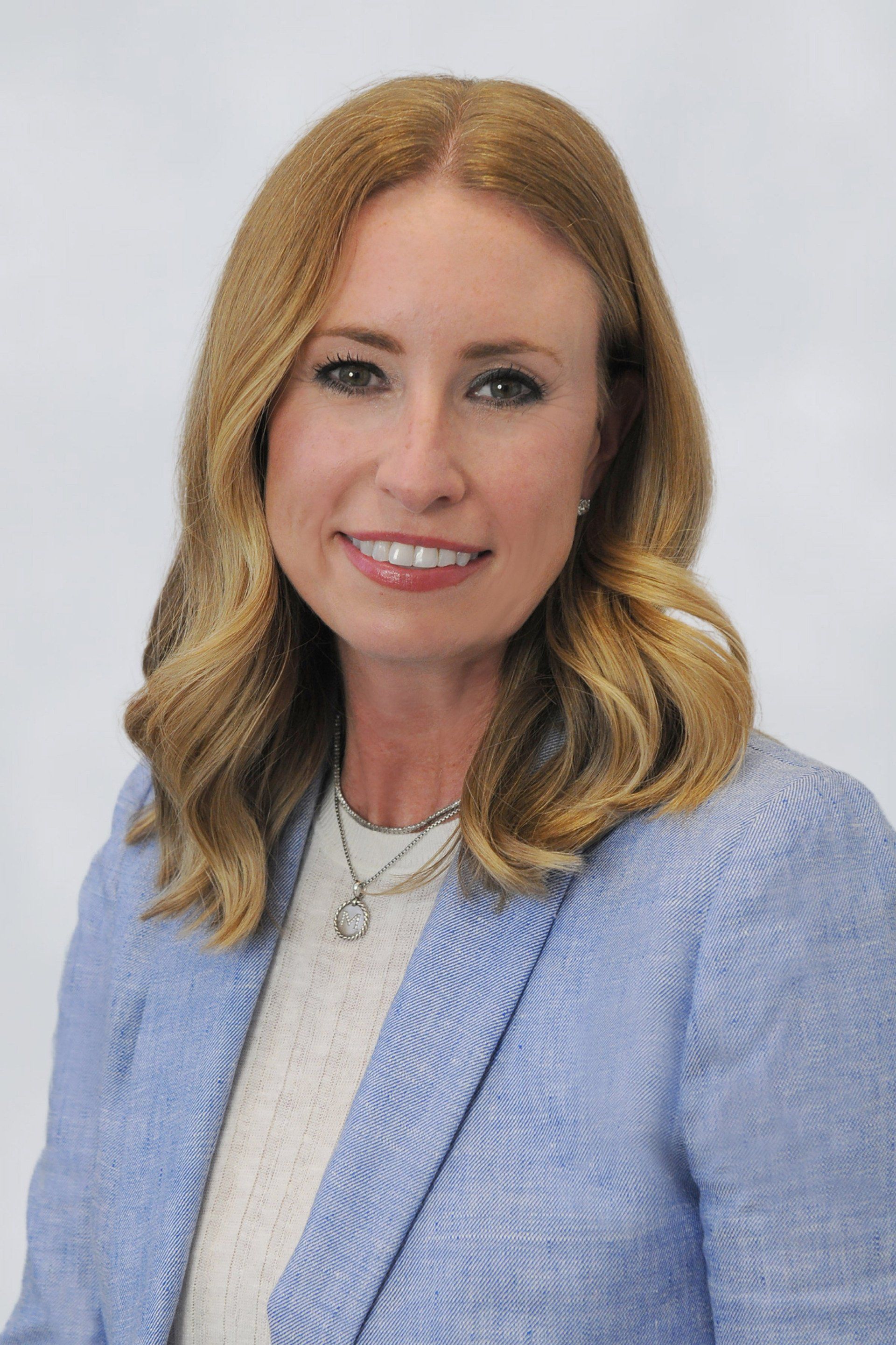 A woman in a blue jacket and white shirt is smiling for the camera.