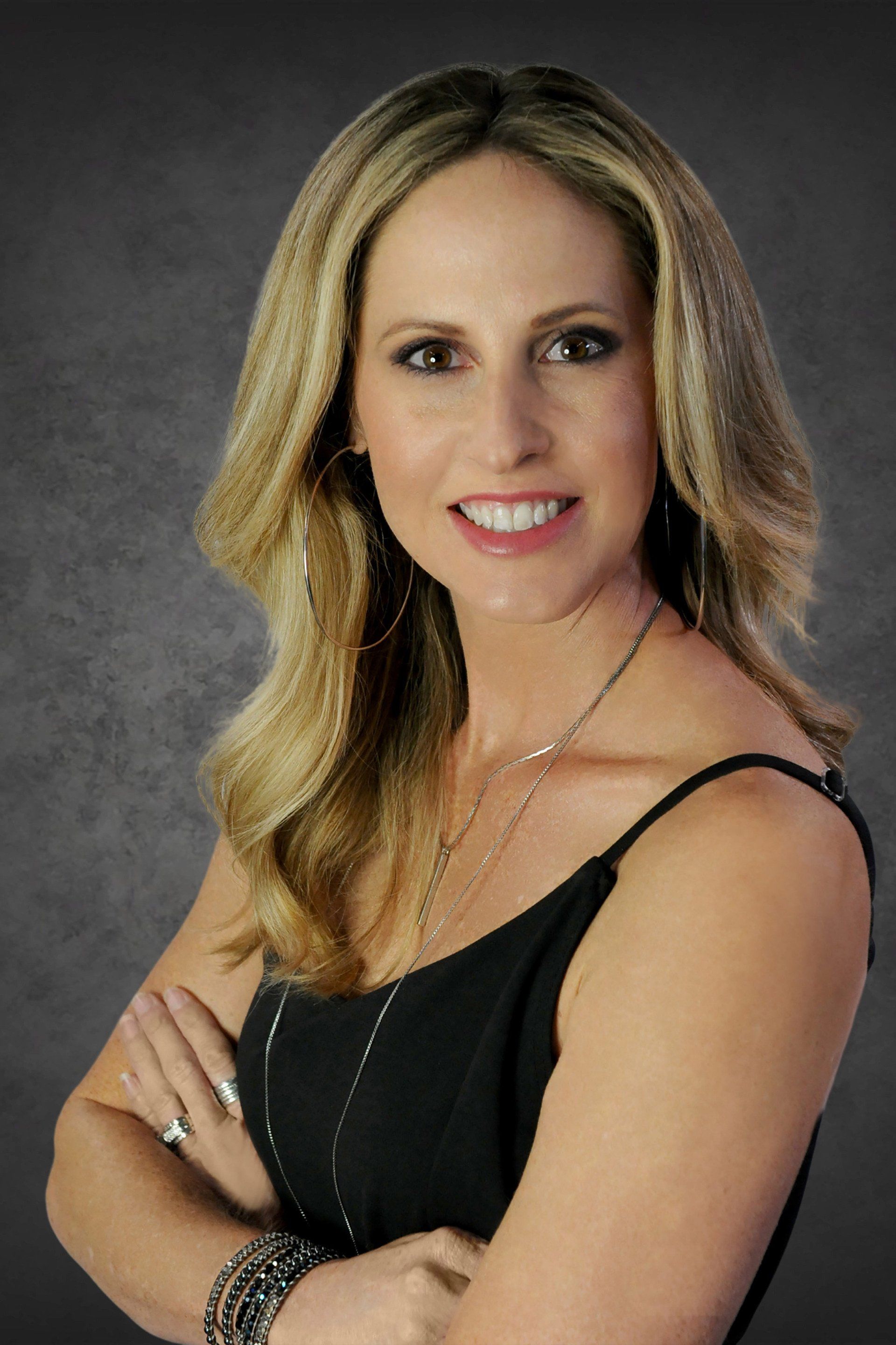 A woman in a black tank top is smiling with her arms crossed.
