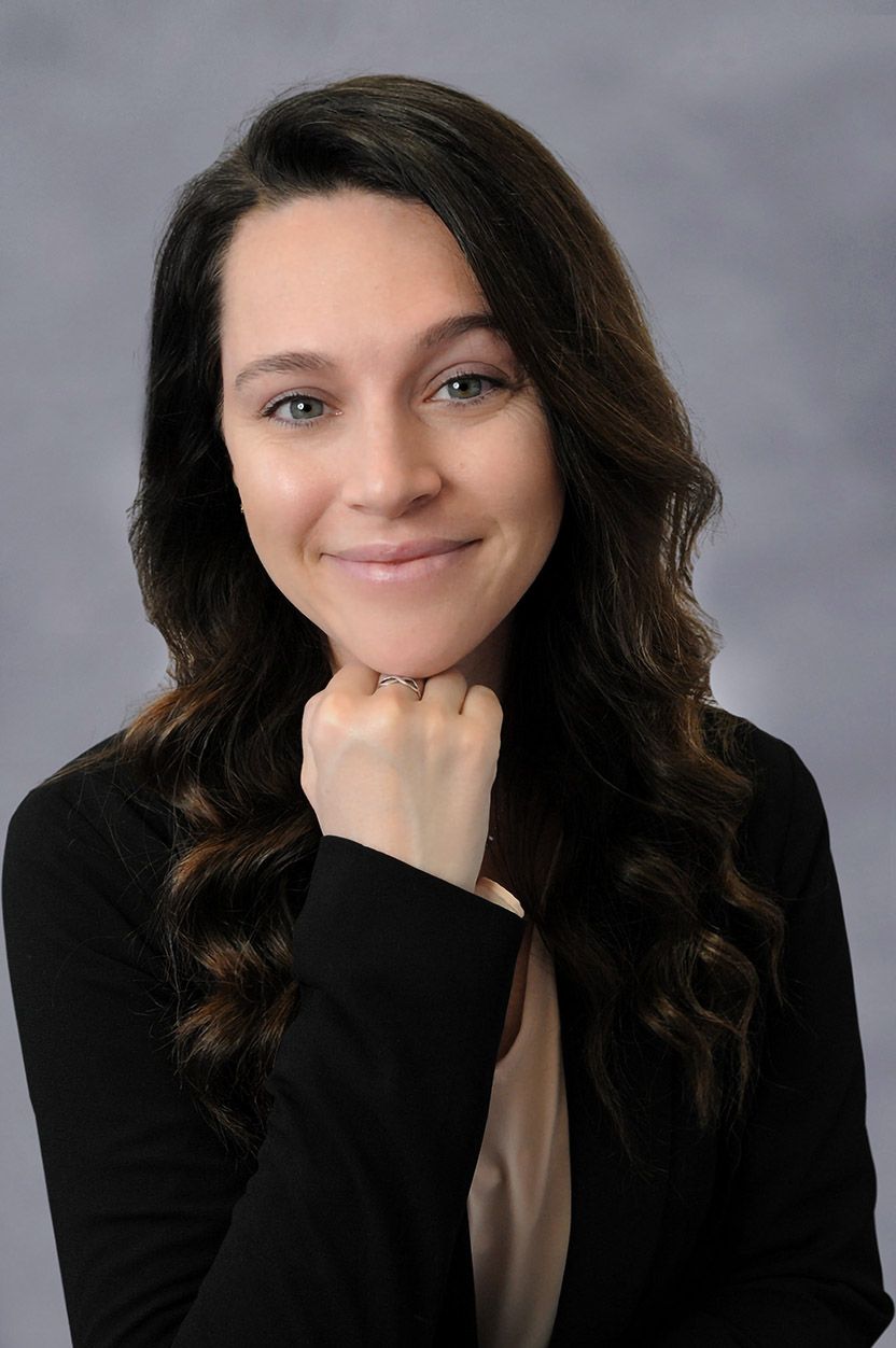 A woman in a black jacket is smiling with her hand on her chin.