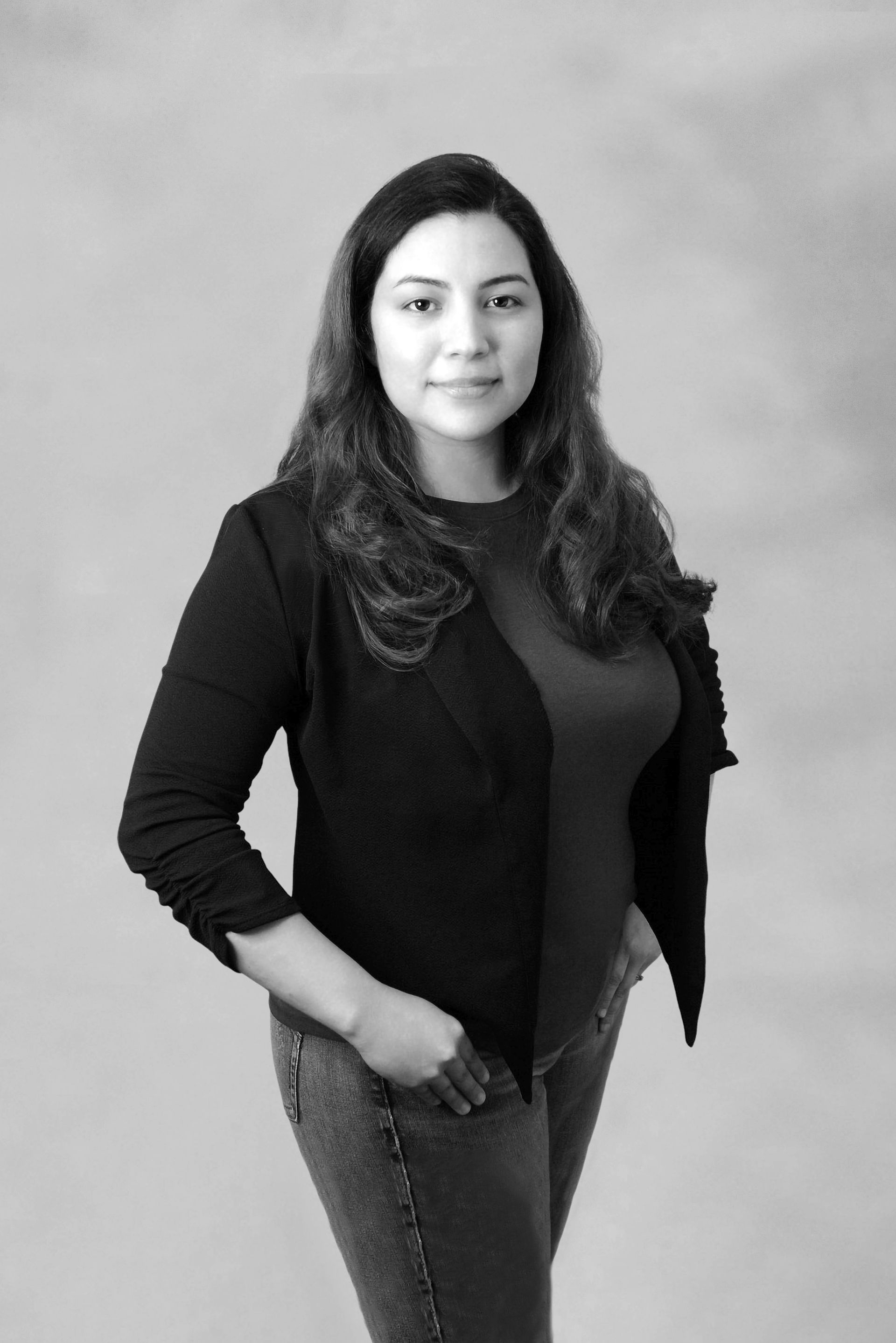 A woman is standing in a black and white photo with her hands in her pockets.