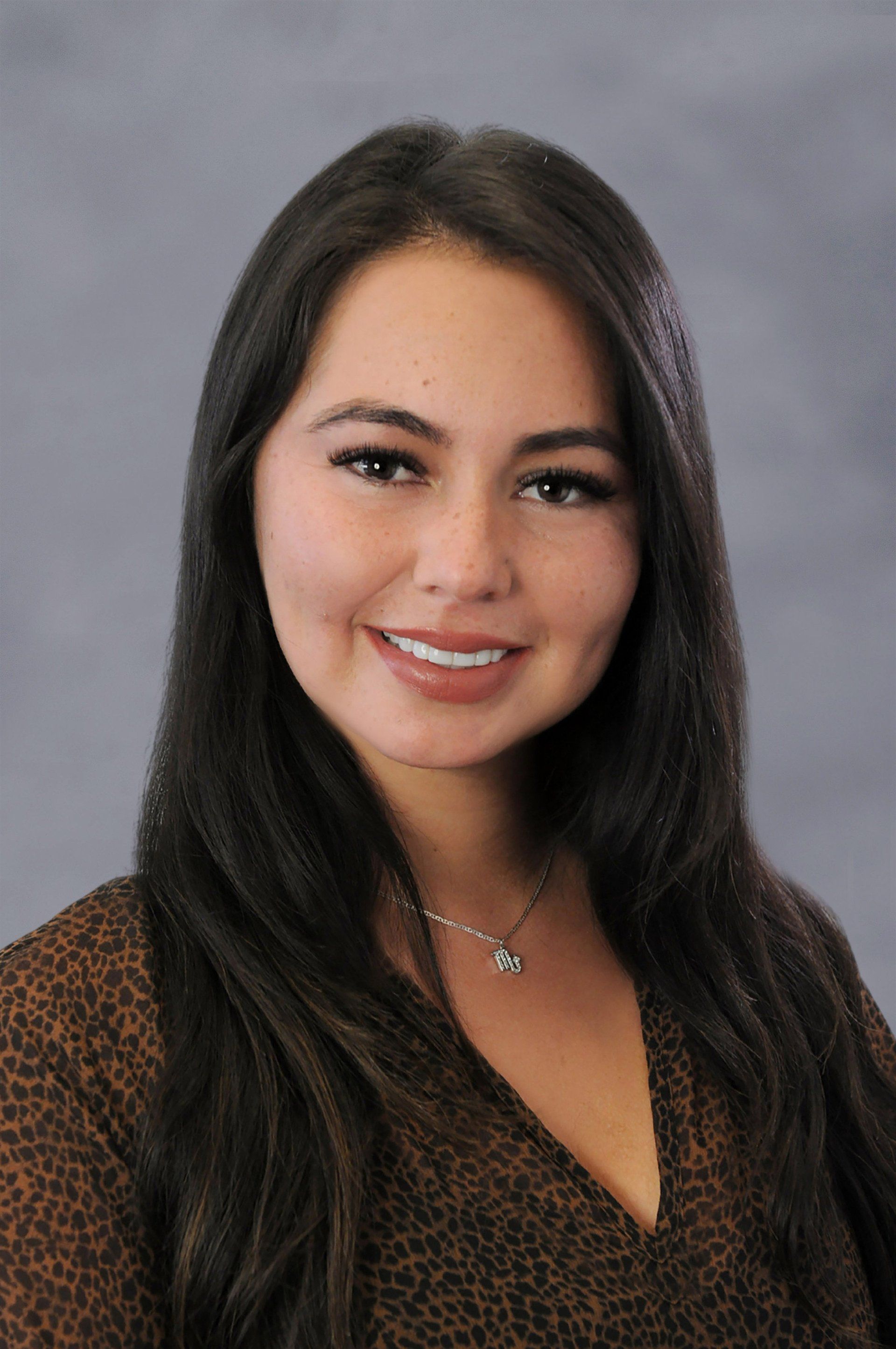 A woman wearing a leopard print shirt and a necklace is smiling for the camera.