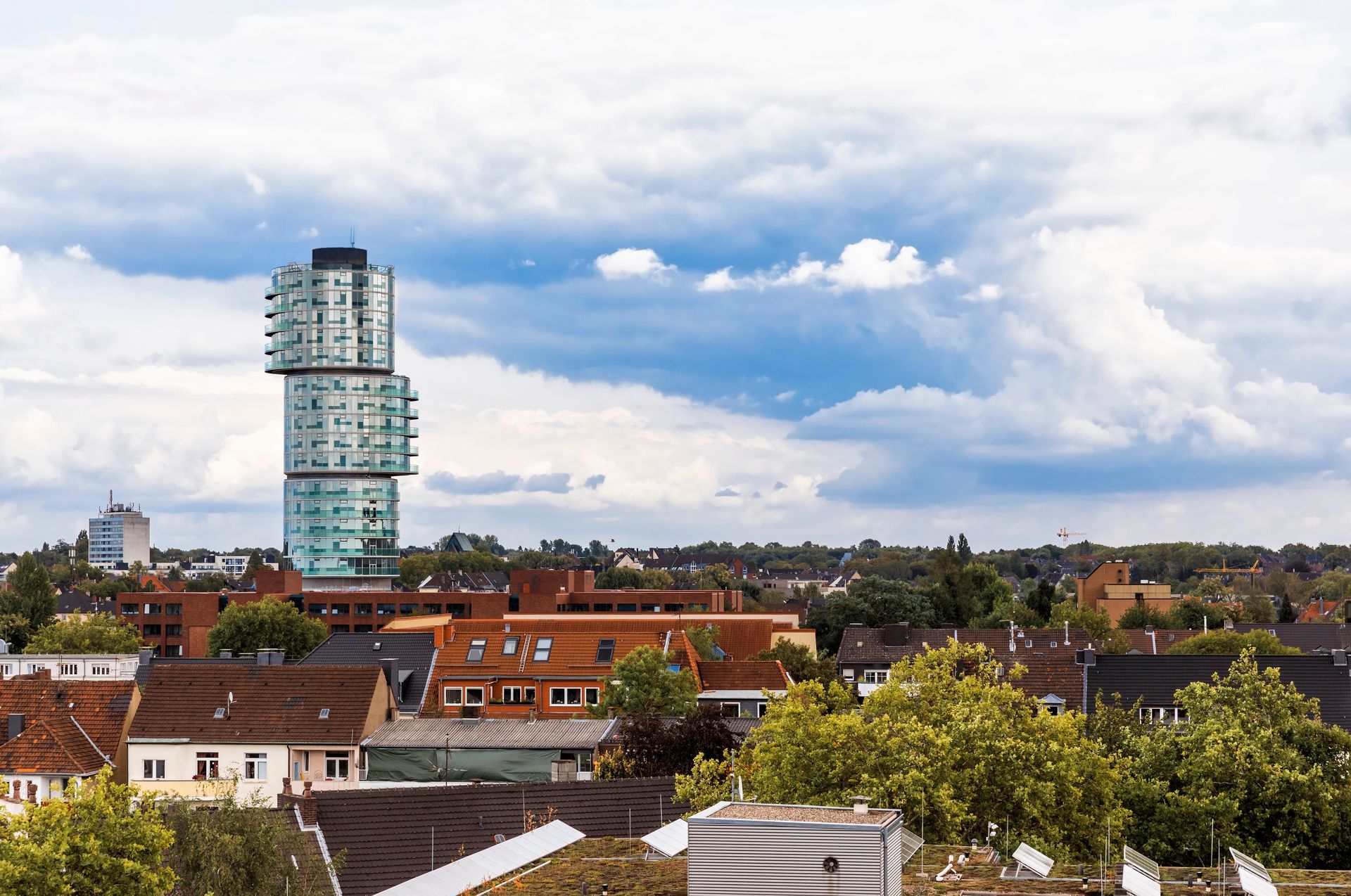 Unter bewölktem Himmel ragt ein modernes Apartmentgebäude über ein niedrig bebautes Wohngebiet.