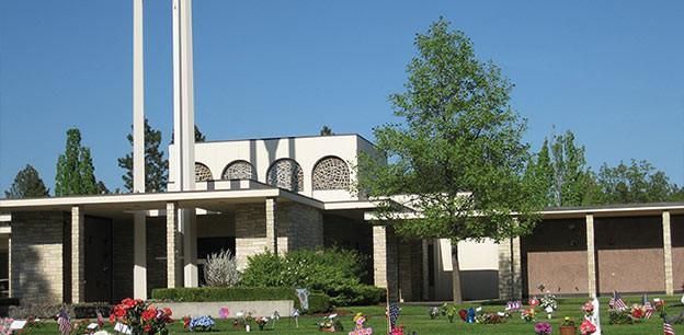 A cemetery mausoleum with tall pillars, white arches, and a lawn filled with memorial decorations under a blue sky.