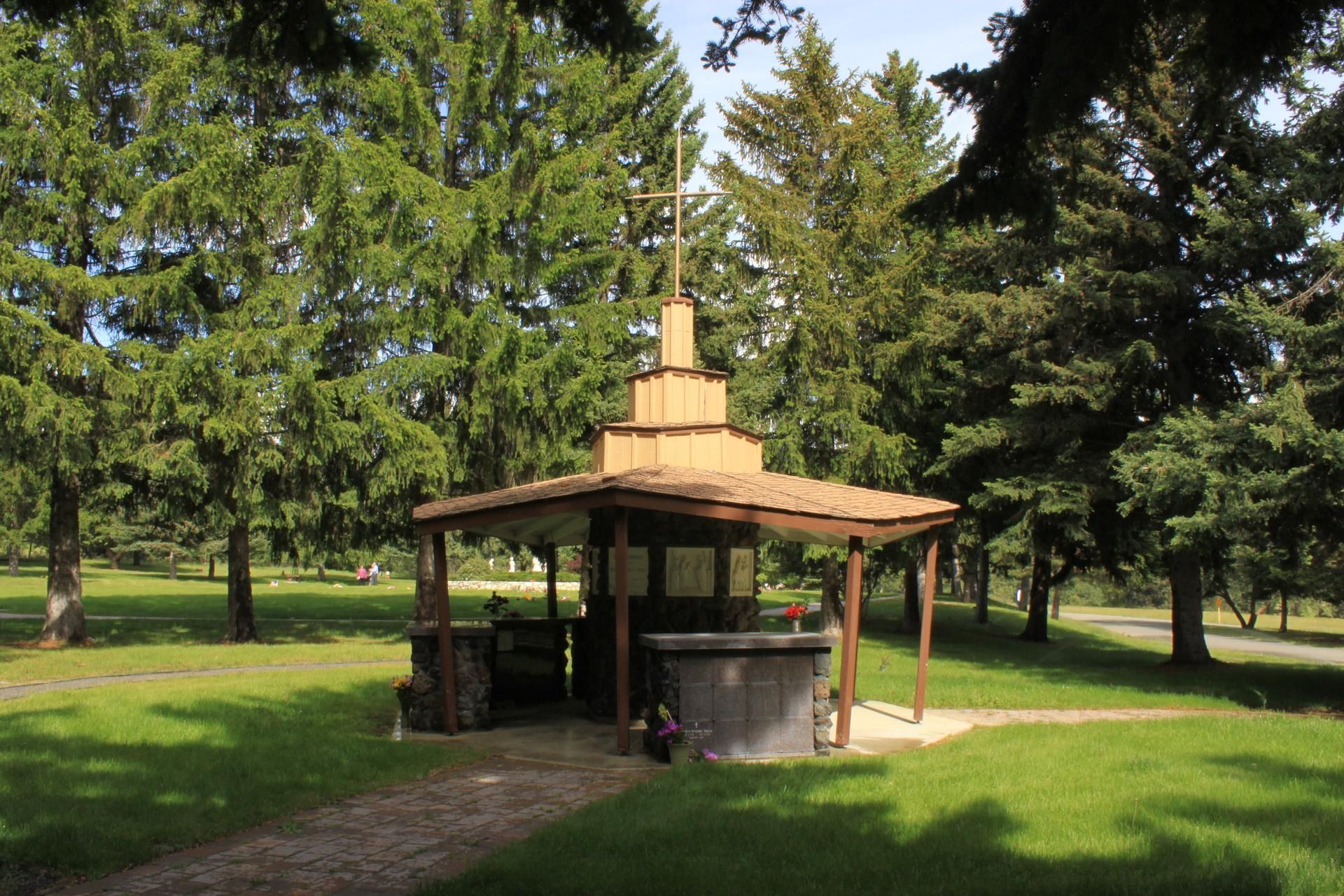 A rustic wooden gazebo with a tiered steeple in a lush, green, sunlit park.