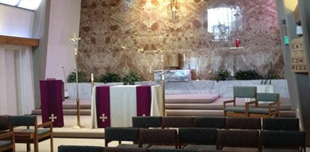 The interior of a church featuring an altar and a podium draped in purple, positioned against a decorative stone wall.