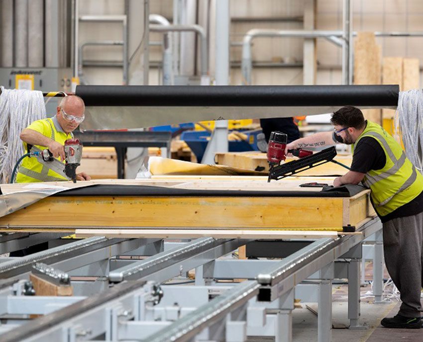 A group of men are working on a piece of wood in a factory.
