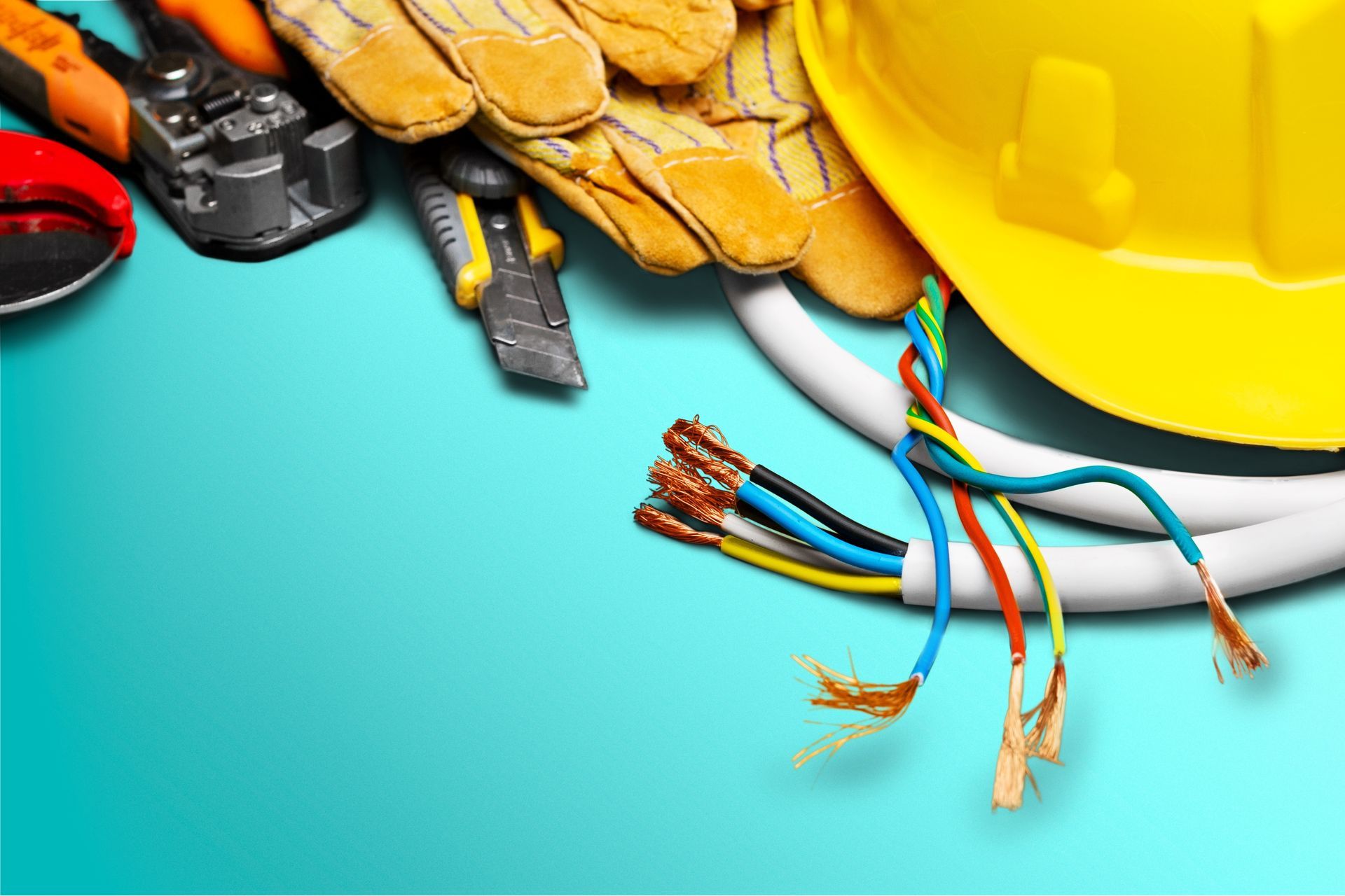A yellow hard hat , gloves , pliers , and a bunch of wires on a blue surface.