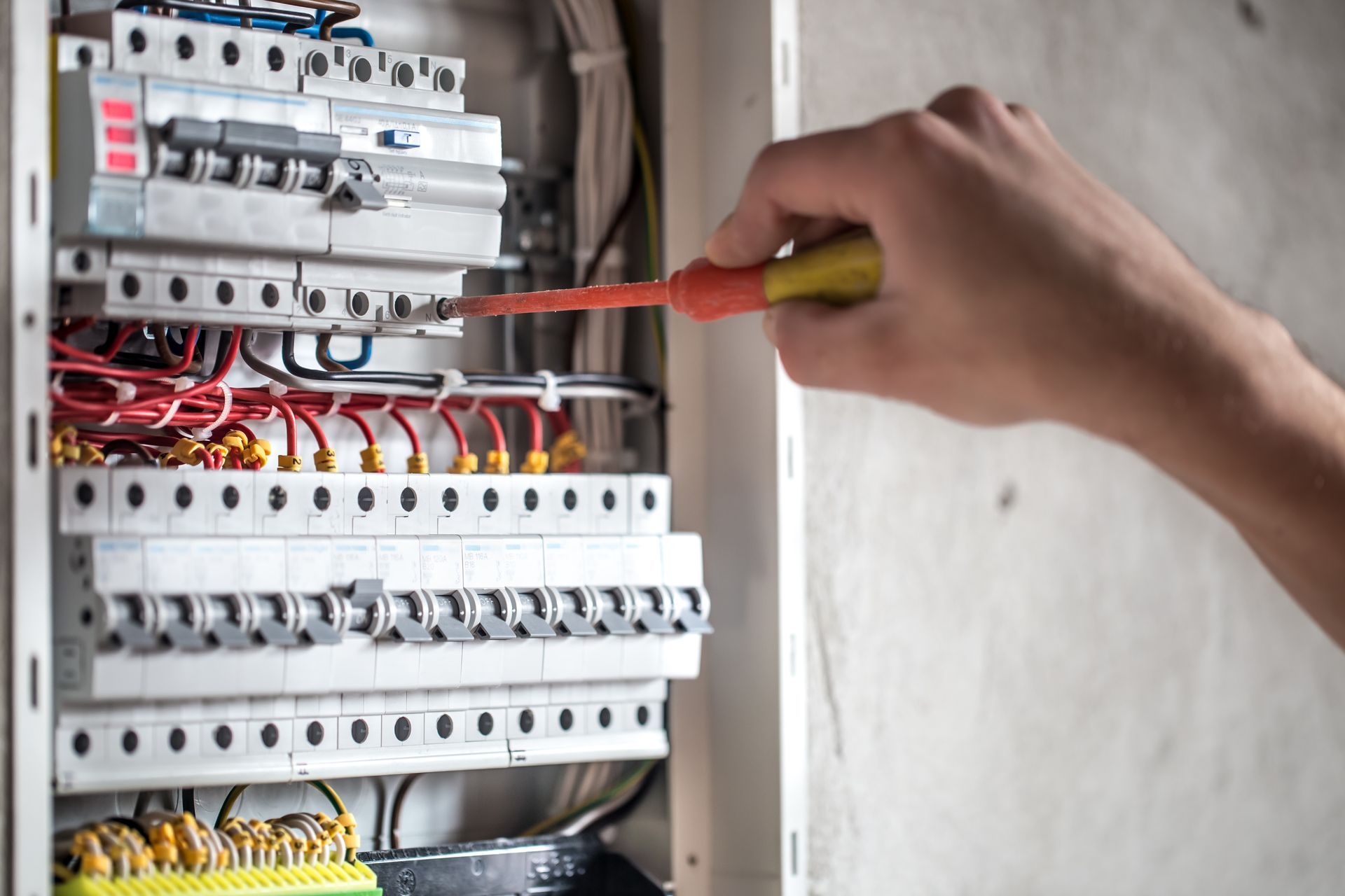 A person is working on an electrical box with a screwdriver.
