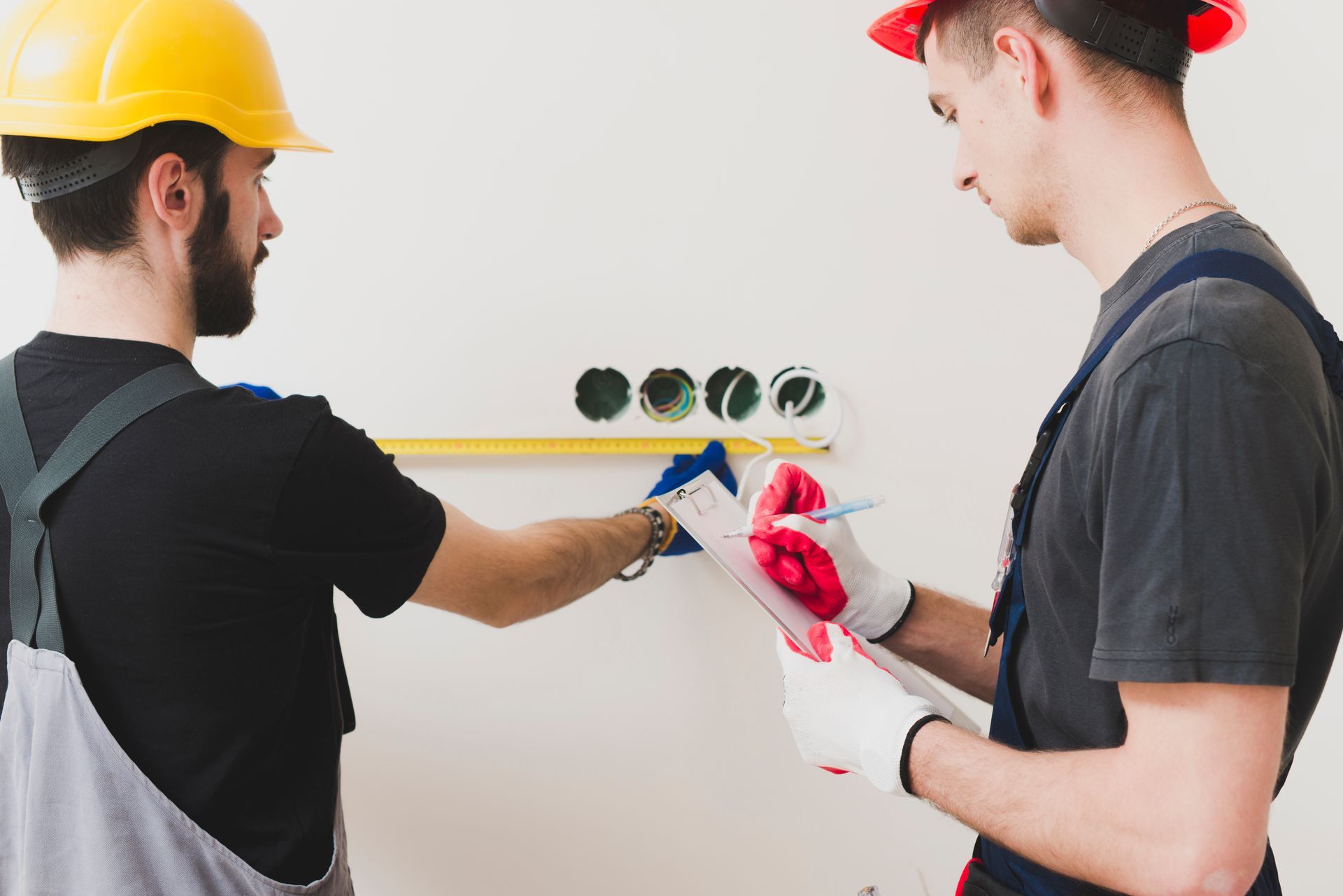 Two construction workers are measuring a wall with a tape measure.
