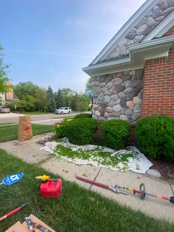 A lawn mower is sitting on the sidewalk in front of a brick house.