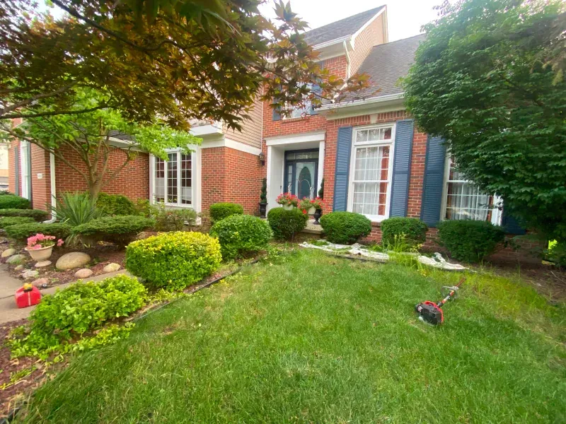 A brick house with blue shutters and a lush green lawn.