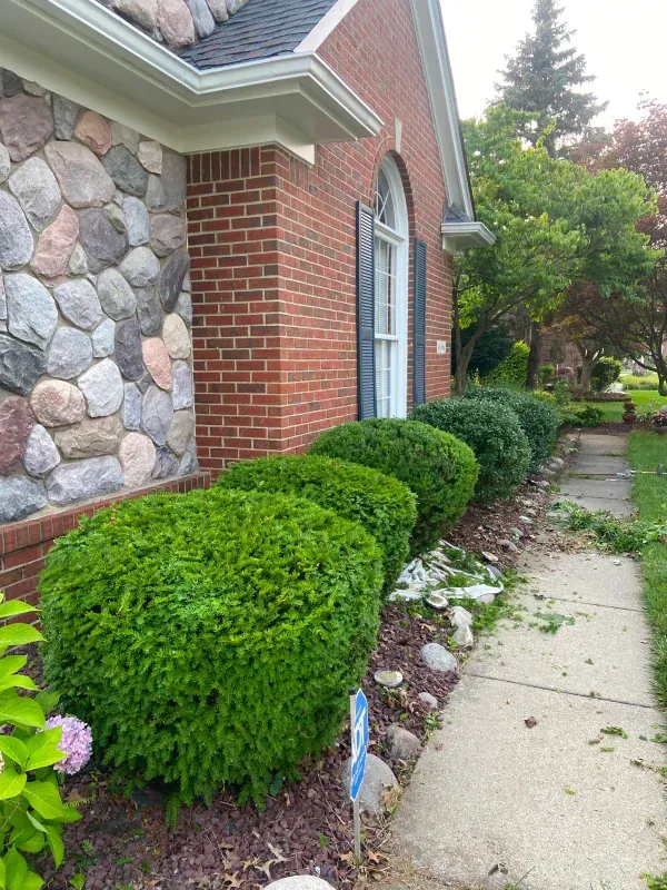 A brick house with a stone wall and bushes in front of it