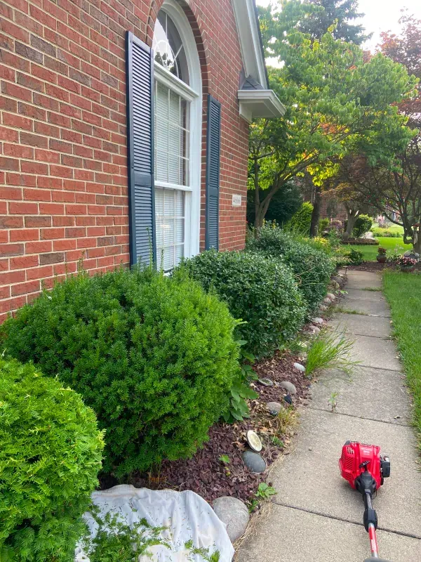 A lawn mower is sitting on the sidewalk in front of a brick house.