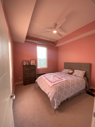A bedroom with pink walls , a bed , a dresser and a window.