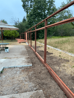 A wooden fence surrounds a patio with a table and umbrellas.