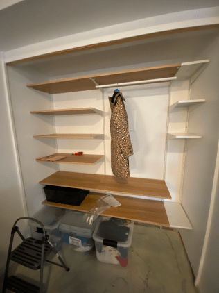 A closet with shelves and a coat hanging on the wall.
