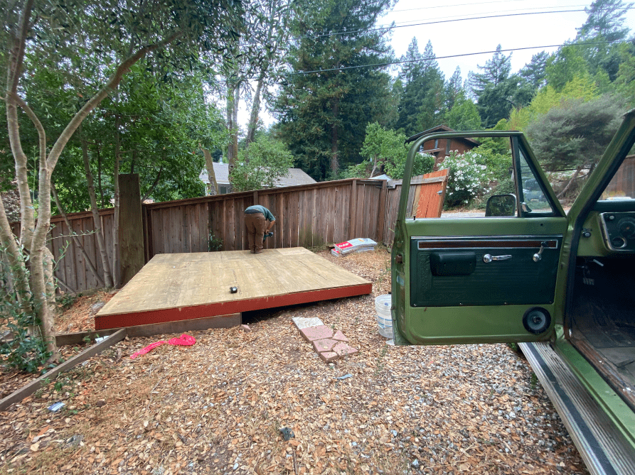 A green truck is parked in a gravel lot next to a wooden platform.