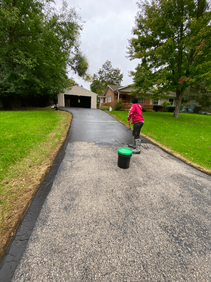 A woman is painting a driveway in front of a house.