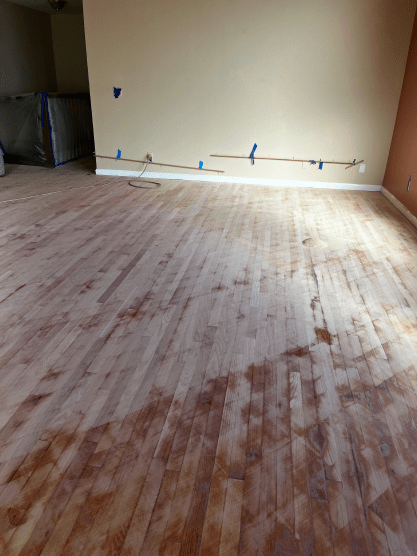 A wooden floor in a room with tape on the wall