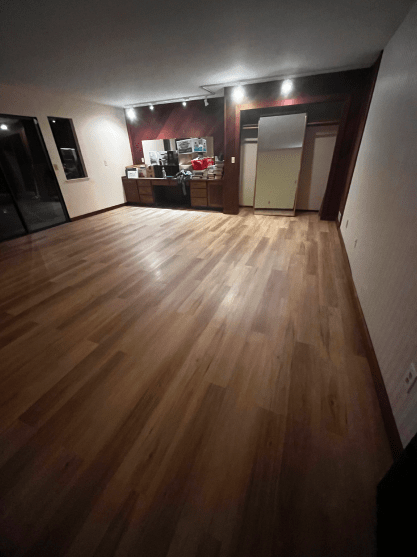A living room with hardwood floors and a kitchen in the background.