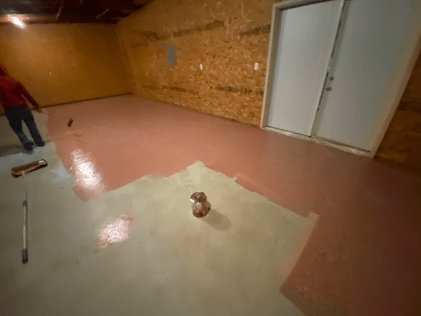 A person is painting a pink floor in a basement.
