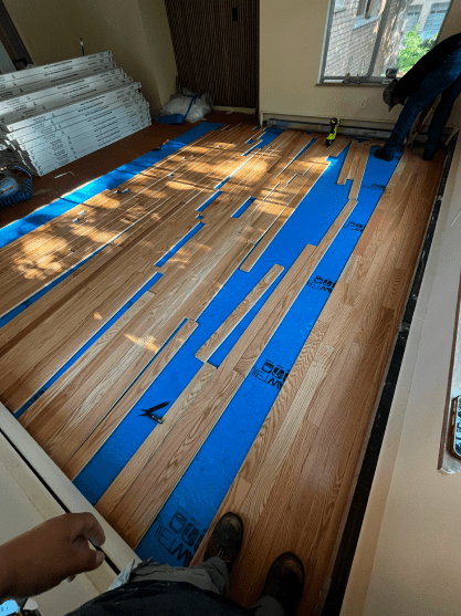 A person standing on a wooden floor with blue tape on it