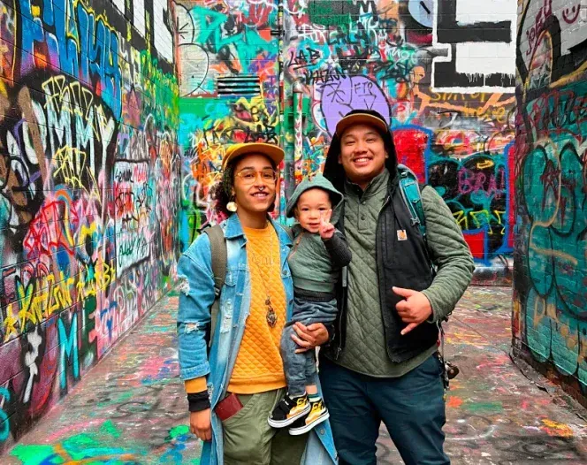 A man and two children are standing in front of a graffiti covered wall.