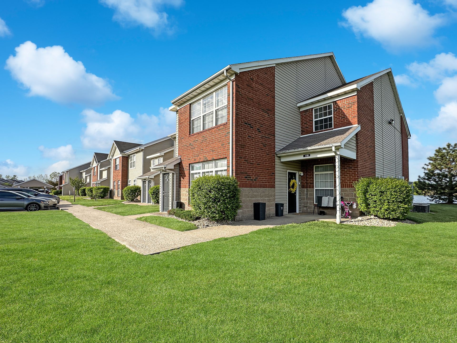 Two-story brick apartment building on a sunny day, surrounded by green grass and blue sky.