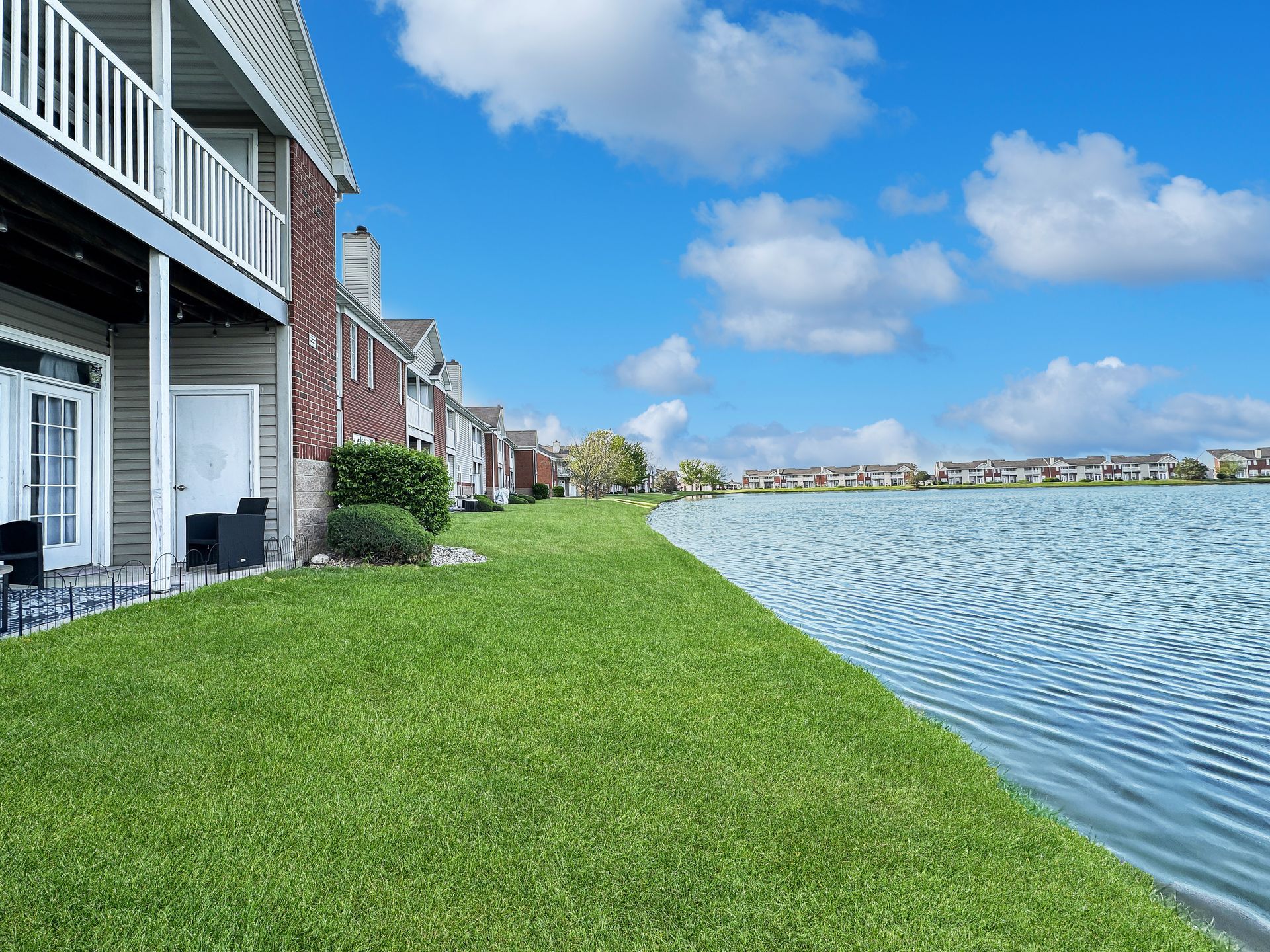Lakeside apartment complex with green grass, blue sky, and water.