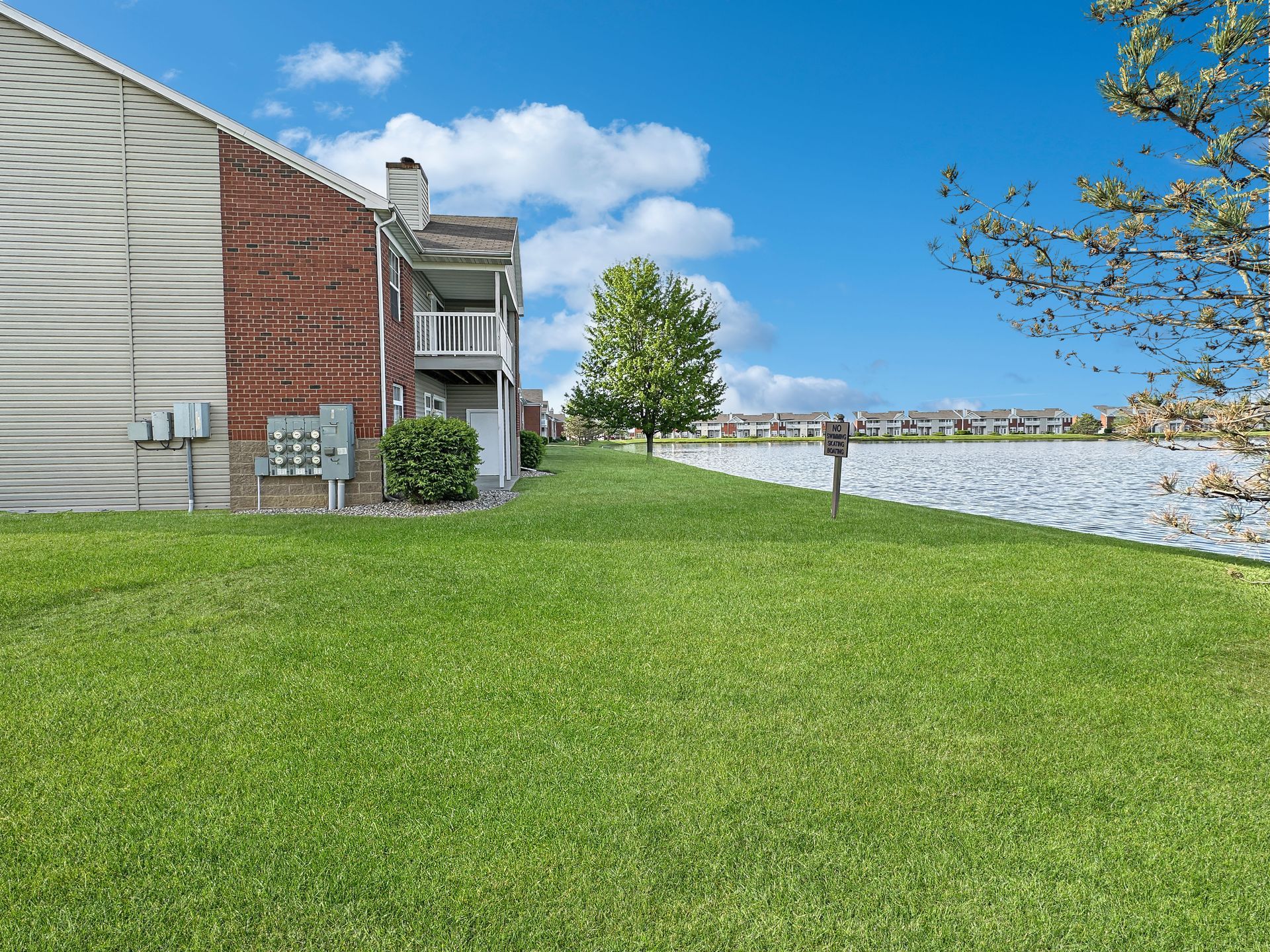 Lush green lawn beside a building with red brick and a lake under a bright blue sky with clouds.