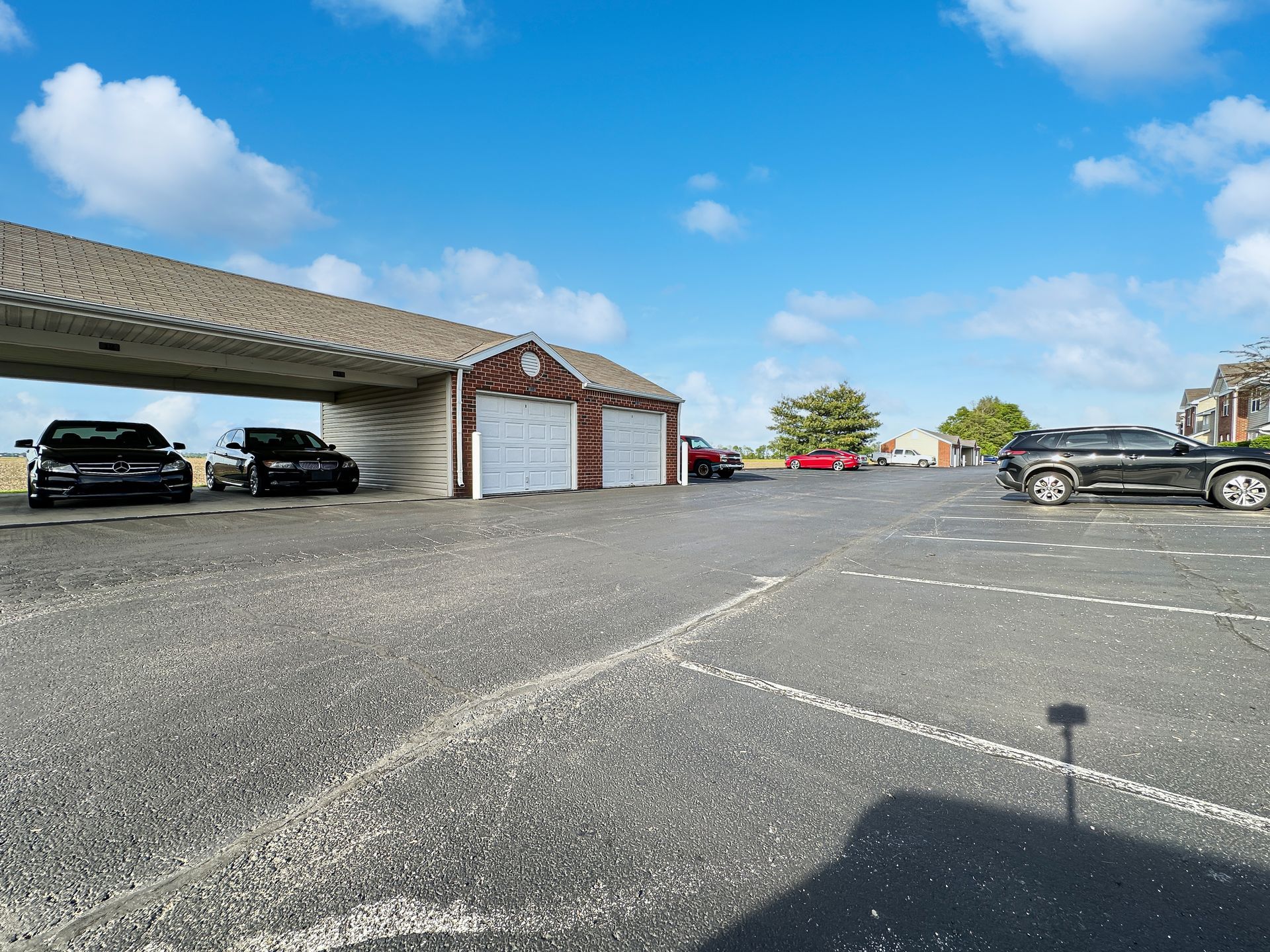 A parking lot with cars under a covered area and in front of a small brick building under a blue sky.
