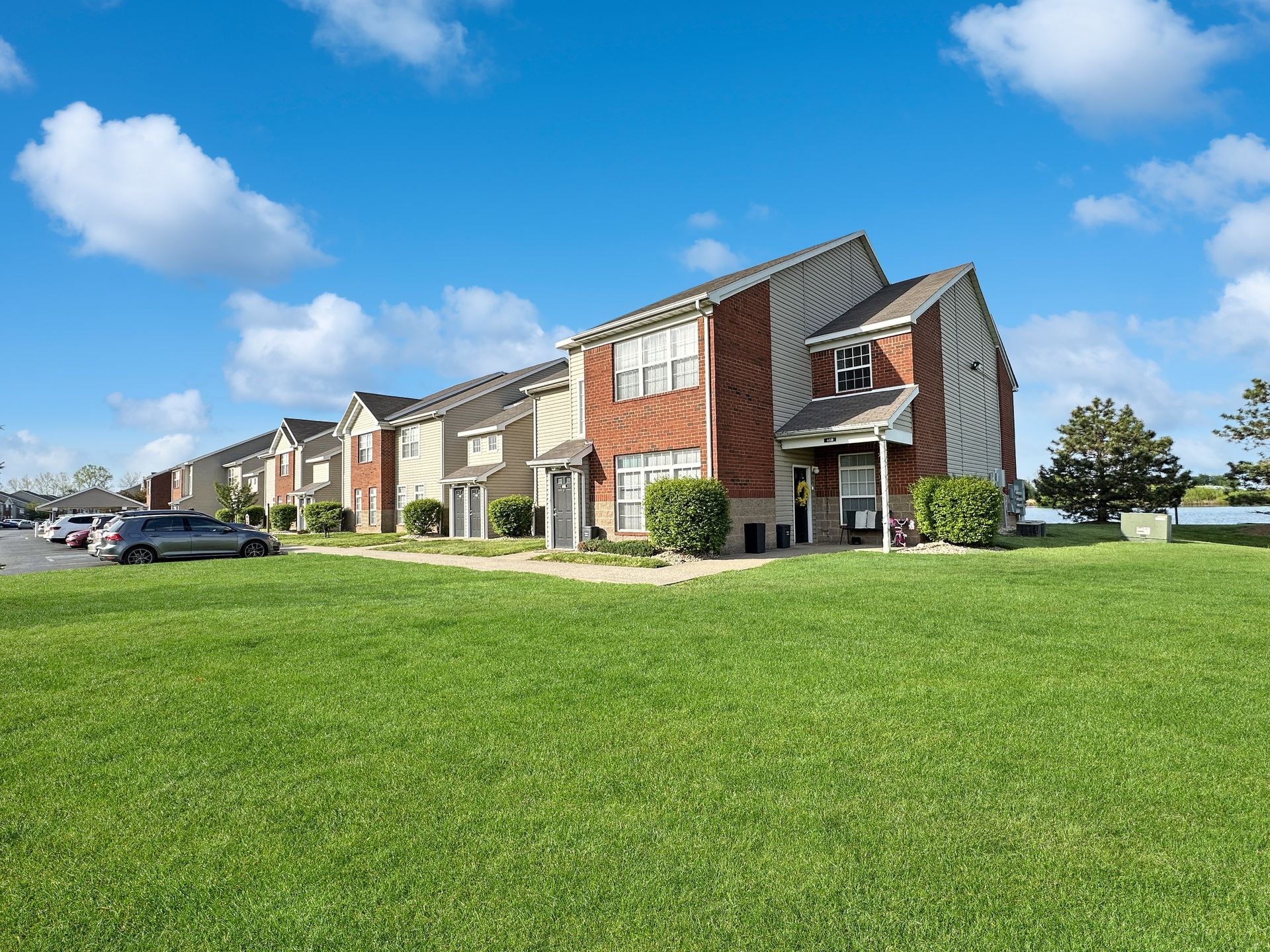 Row of townhouses with brick accents and green lawn under a blue sky.