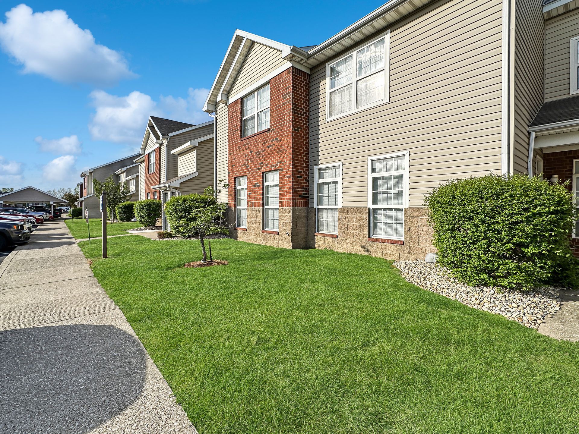 Row of tan and brick townhomes with green lawn and blue sky.